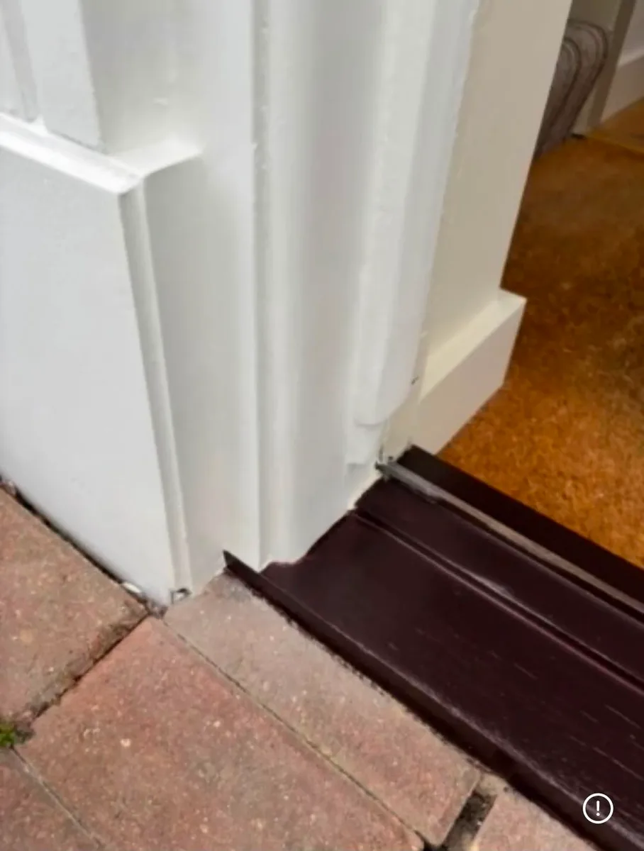 After photo of a repaired exterior door frame in Tampa: jamb and casing bottom sanded, primed, and repainted white on a new dark-bronze aluminum threshold over brick pavers, with no trace of the rot repair