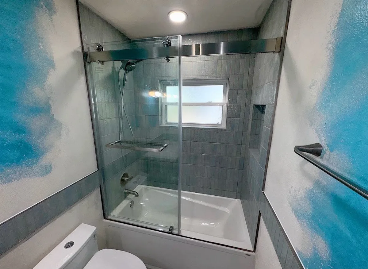 Finished Tampa bathroom renovation with a frameless sliding glass tub door, vertical aqua tile surround, tiled niche, and a matching accent band around the room