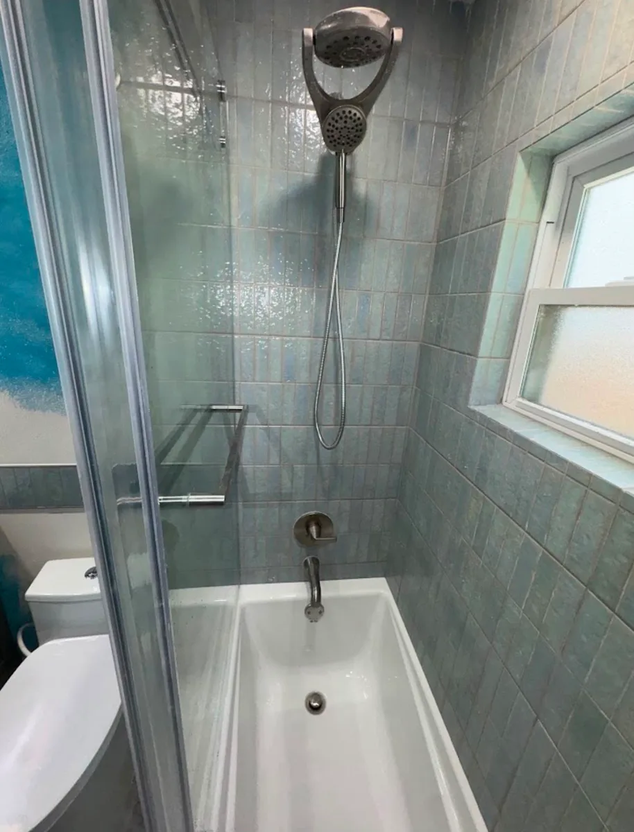 After photo of a Tampa tub surround rehab with sea-glass blue-green 2x8 tile stacked vertically to the ceiling, brushed-nickel rain and hand shower, and a new white tub