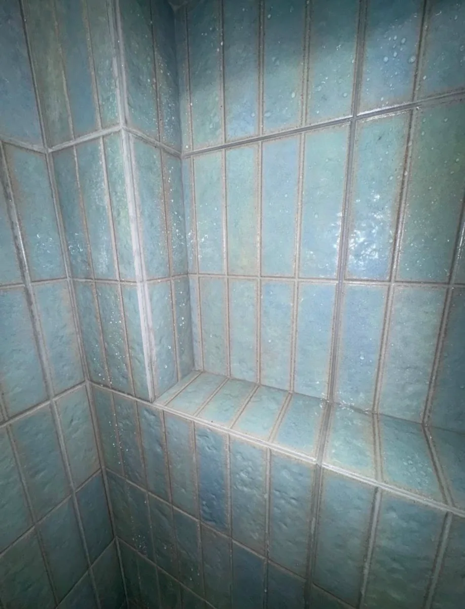 After detail of a Tampa tub surround remodel: sea-glass aqua 2x8 tile stacked vertically with a built-in shower niche and light gray grout lines