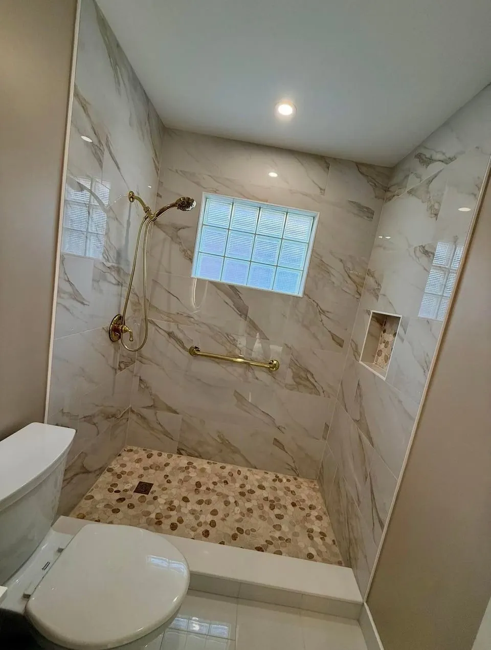 Completed walk-in shower remodel with marble-look tile, pebble floor and gold fixtures — Fenelon Handyman Services, Tampa Bay, FL