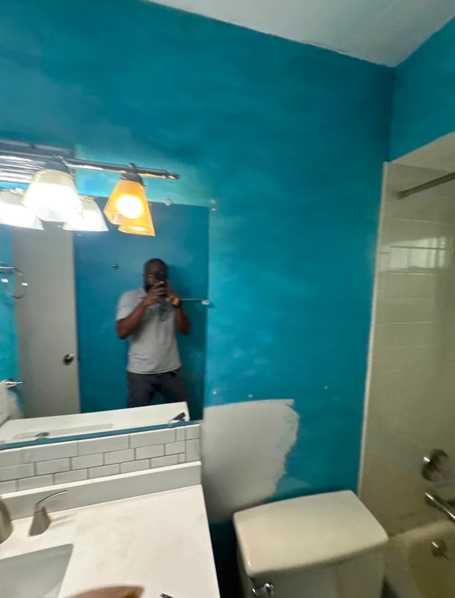 Fenelon Handyman Services owner in a Tampa bathroom before the tub surround makeover, with turquoise walls, an existing white subway backsplash and the old vanity light bar