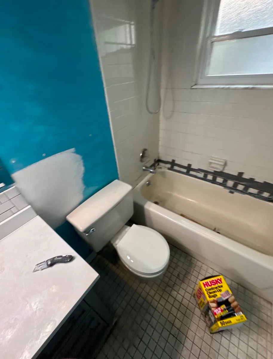 Angled before view of a Tampa hall bathroom tub surround remodel showing old 4x4 tile, toilet, tub, tape line at the seam, and original mosaic tile floor