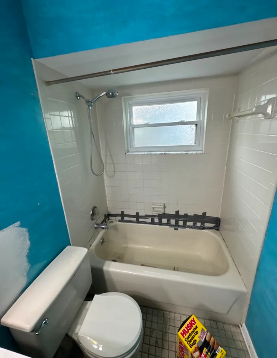 Before photo of a Tampa hall bathroom tub surround with dated cream 4x4 tile, an almond bathtub, and a black tape line marking the failed caulk seam
