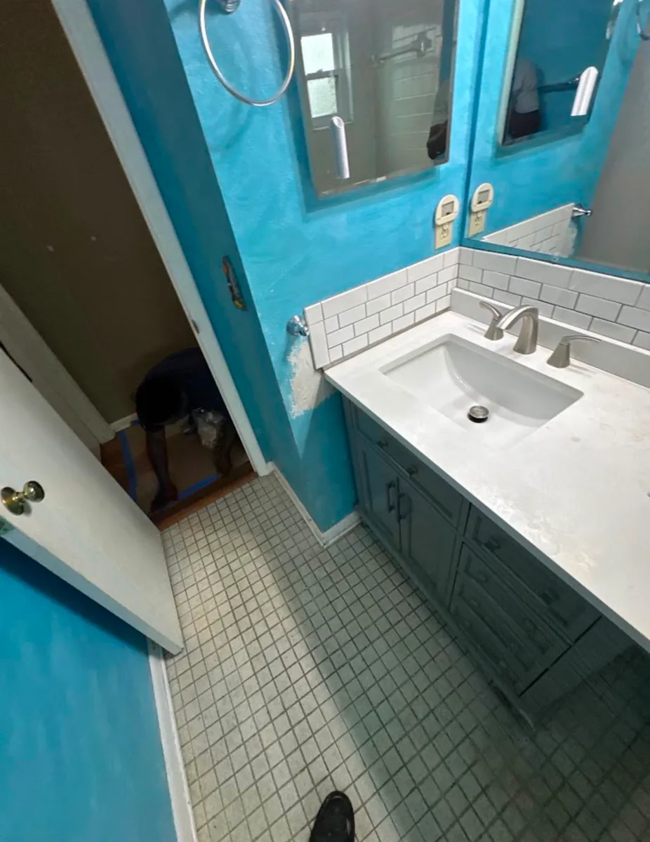 During a Tampa bathroom renovation: new gray vanity with white quartz-look top and brushed-nickel faucet set against turquoise walls, original mosaic tile floor still in place